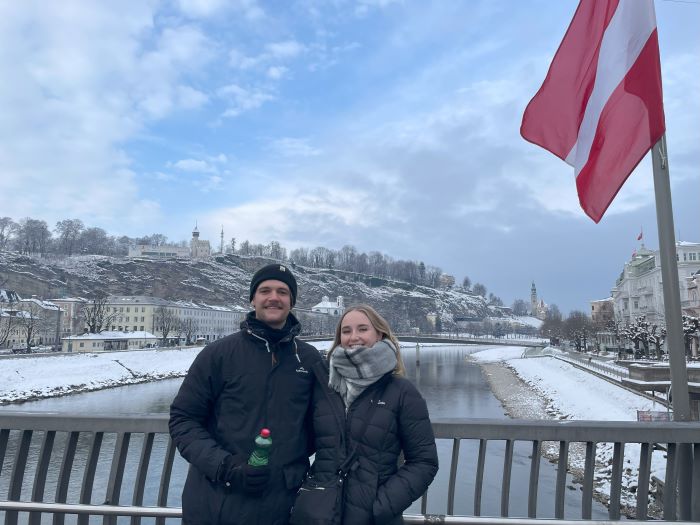 couple on a bridge with a river and snow covered town behind them